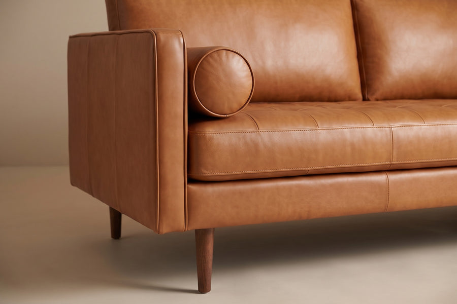 Menton 88" Cognac Leather Bench-Seat Sofa: close-up of one round leather bolster resting against the track arm, with a tapered walnut-finish leg below