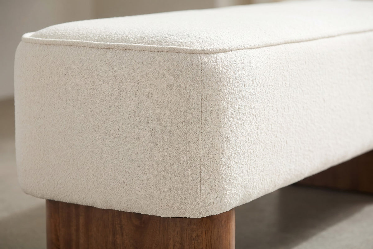 Close-up of one rounded corner of the cream textured fabric and its piped top edge, above one brown rubberwood block leg (Montsouris)