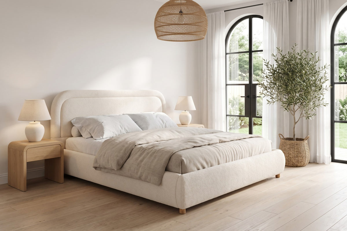 Nina beige-white bouclé platform bed with a rounded headboard in a bright bedroom with tall arched windows