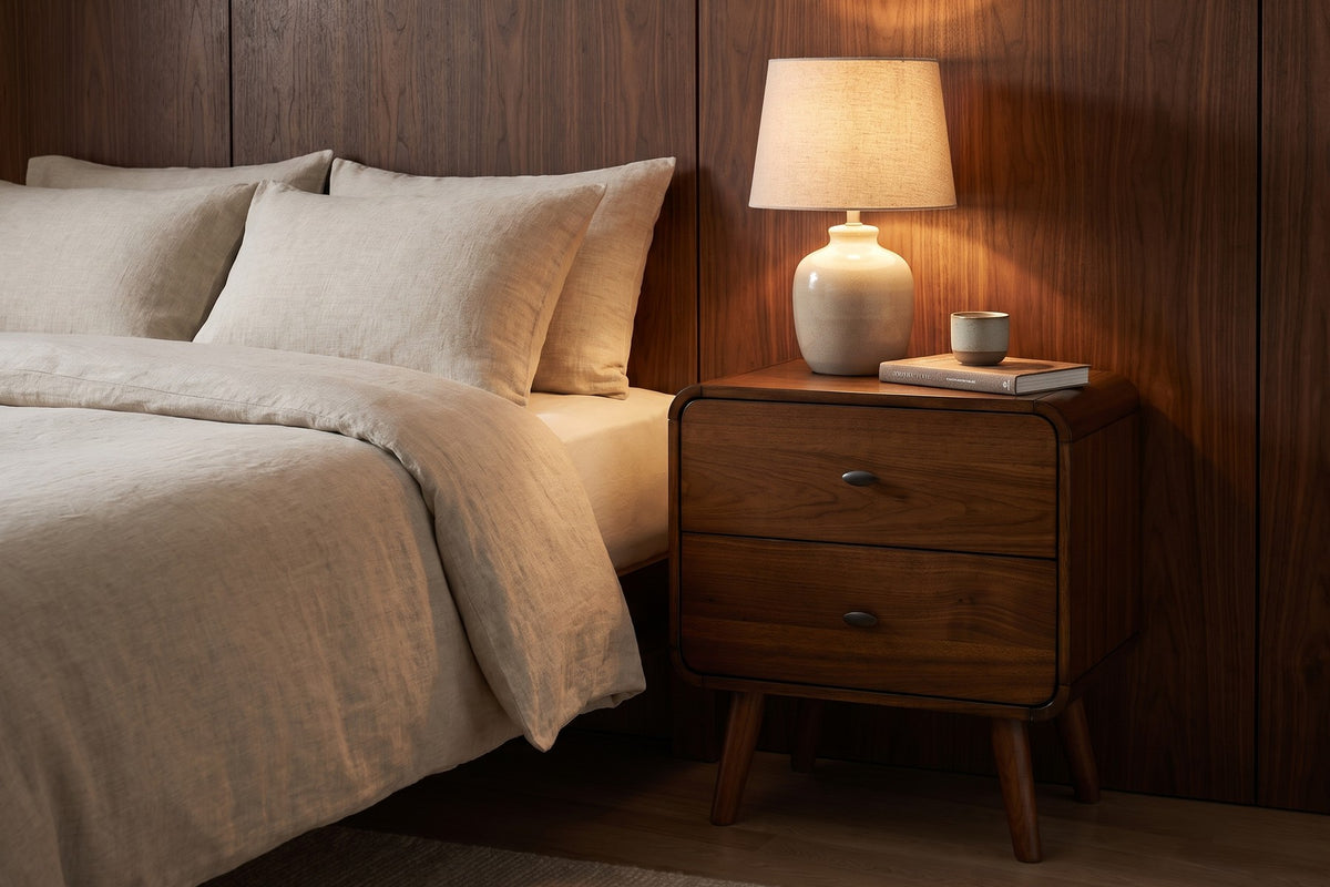 Noémie mid-century dark walnut 2-drawer nightstand in a warm walnut-panelled bedroom in the evening, beside the bed