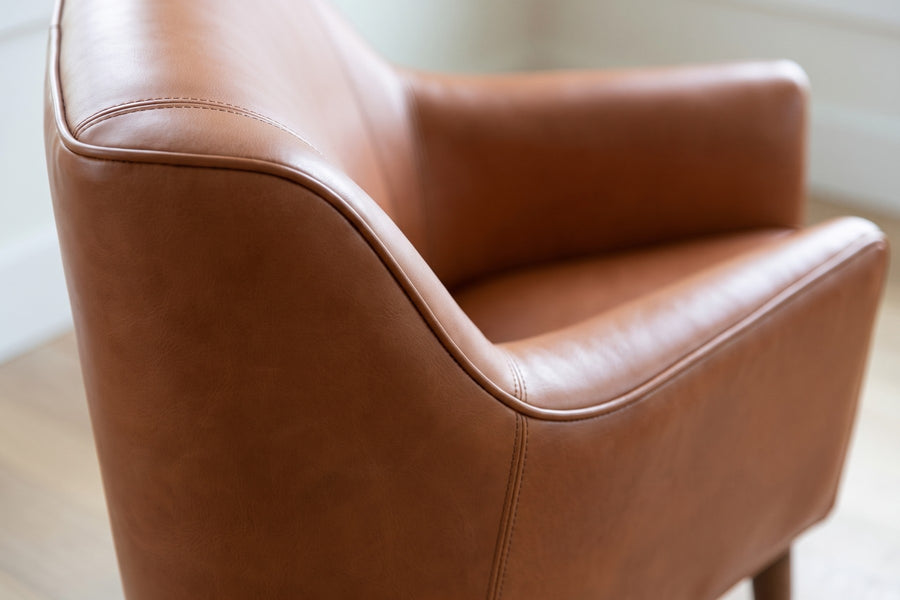 Nyons Cognac Leather Armchair and Ottoman: close-up of the soft curve where the cognac leather back dips down into a slim sloping arm, showing the stitched line along its top
