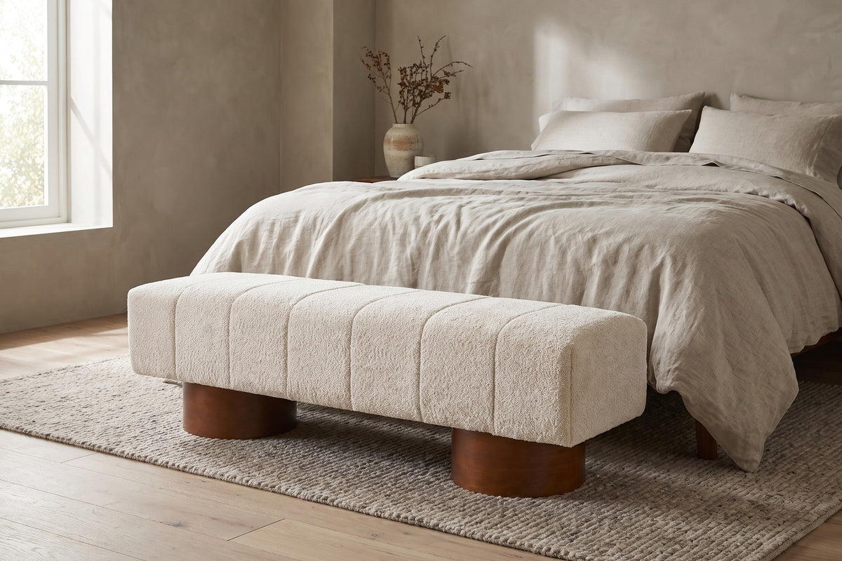 Pigalle cream bouclé channel bench with walnut-tone drum legs at the foot of a bed in a calm bedroom