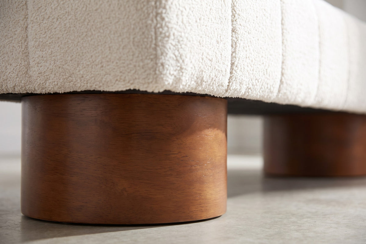 Close-up of one wide round walnut-brown drum leg under the cream boucle bench (Pigalle)