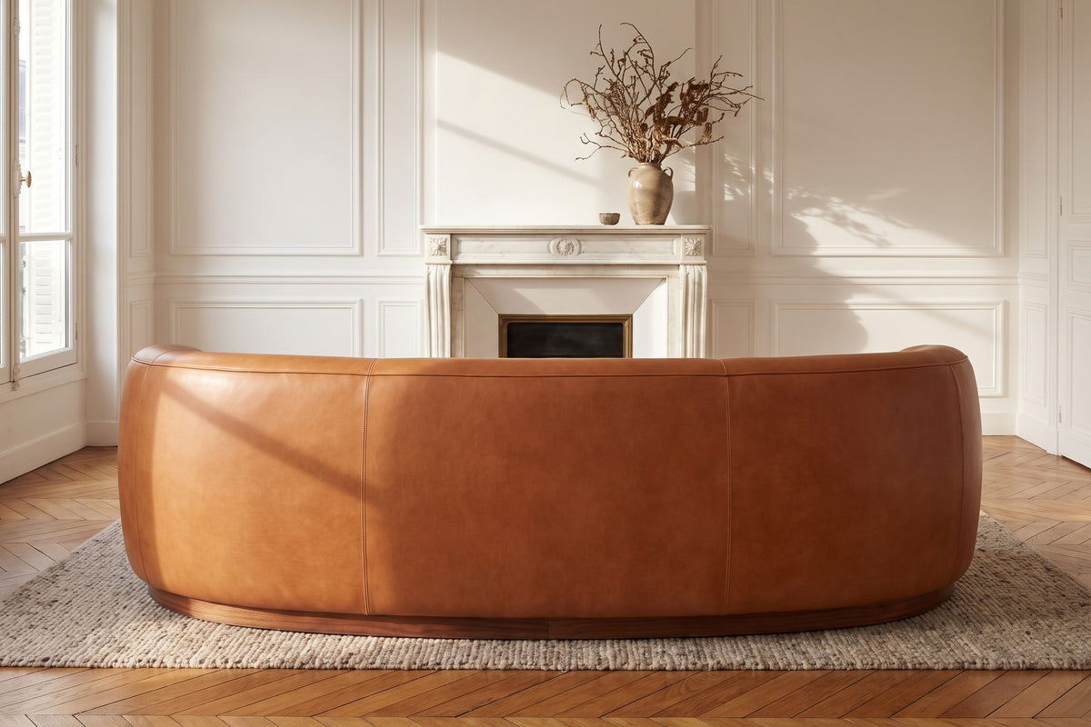 Pornic Cognac Curved Leather Sofa seen from behind, facing a marble fireplace in a Paris apartment