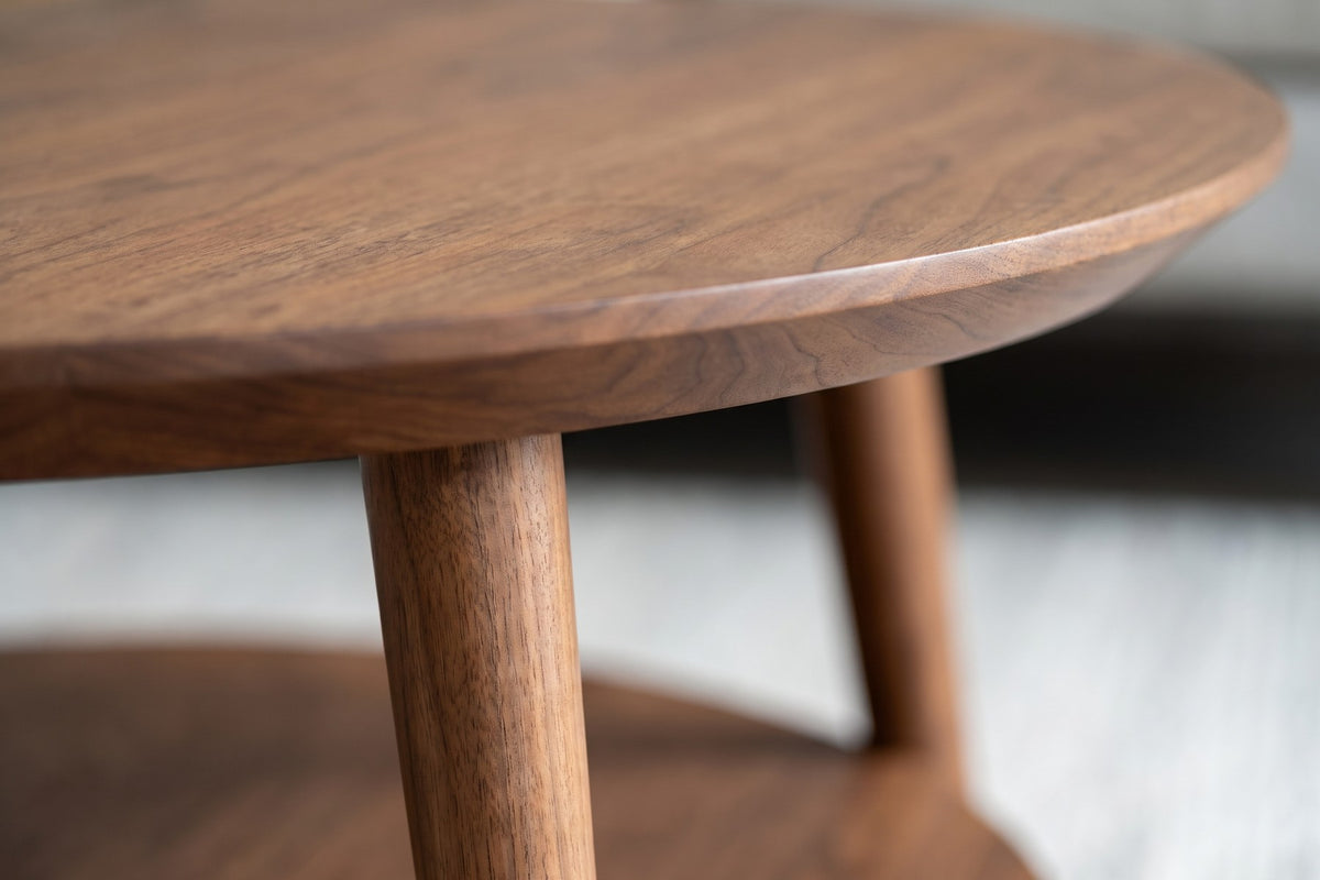 Ramatuelle Walnut Round Coffee Table: close-up of the round top's bevelled underside and slim edge where a splayed leg meets it, walnut grain visible