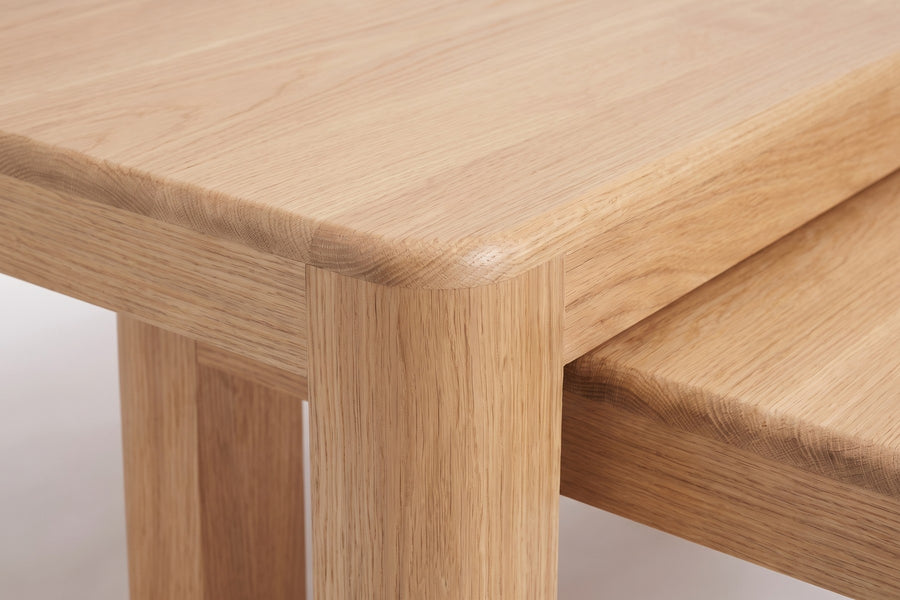 Roussillon Oak Nesting Coffee Tables: close-up of a softly rounded corner of the thick oak top and the rounded square leg below it, oak grain visible