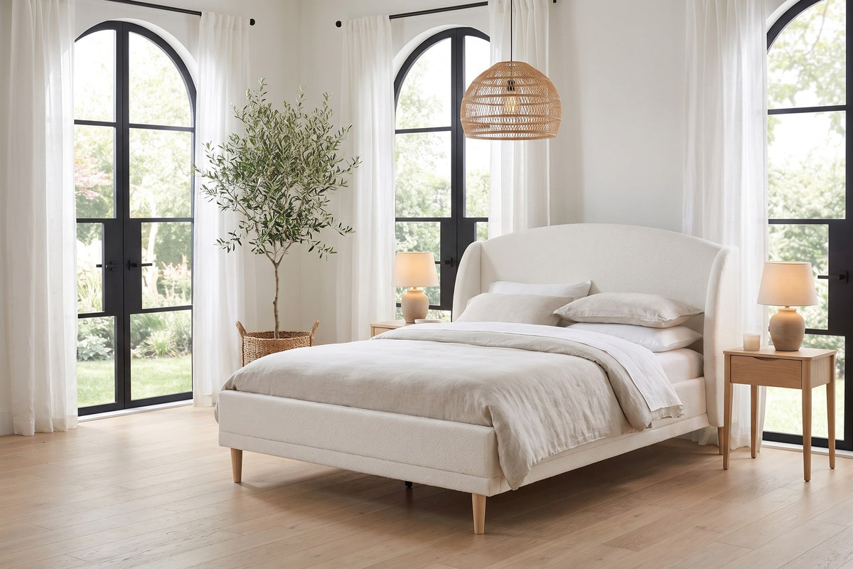 Sabine white bouclé bed with a wingback headboard and tapered wood legs in a bright bedroom with tall arched windows