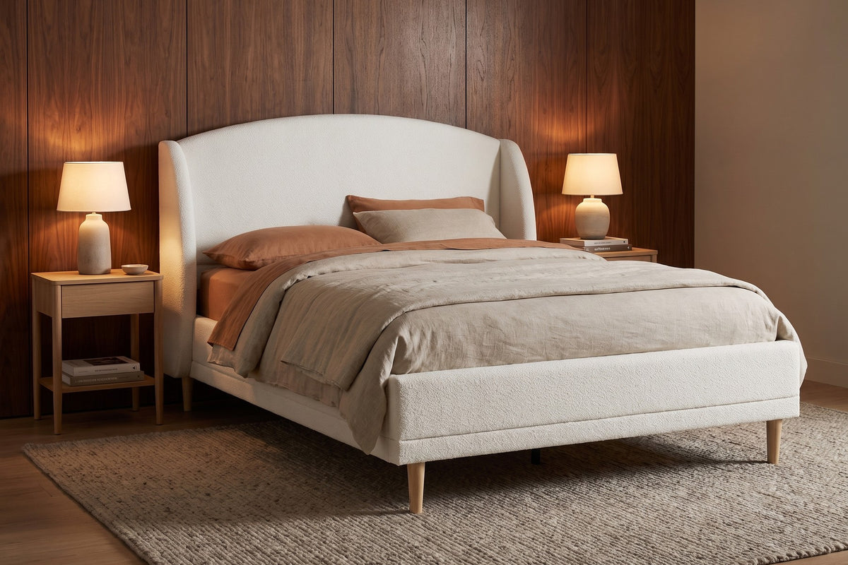 Sabine white bouclé bed with a wingback headboard and tapered wood legs in a warm walnut-panelled bedroom in the evening
