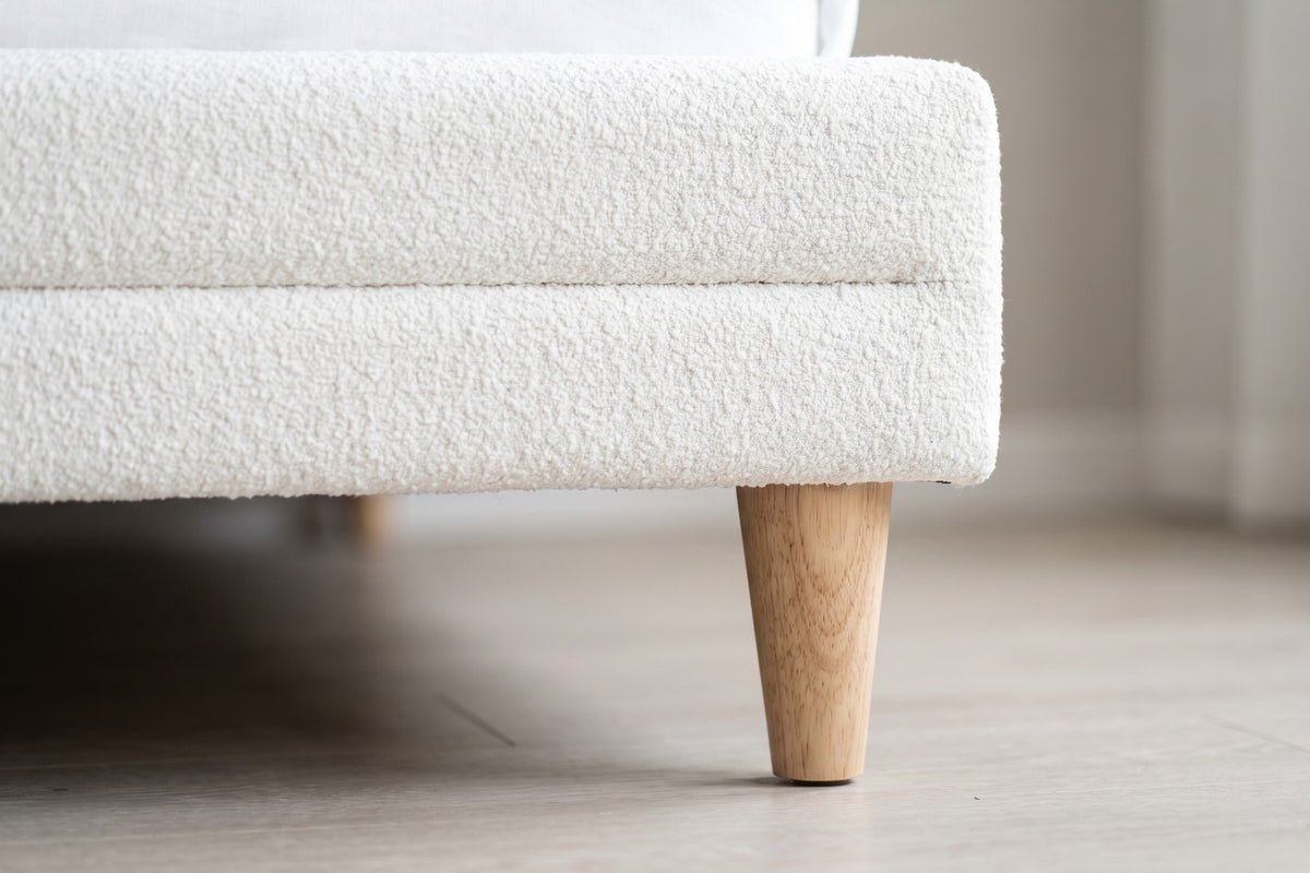 Close-up of one tapered natural-wood leg beneath the white bouclé side rail (Sabine)