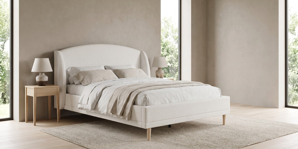 Sabine white bouclé bed with a wingback headboard and tapered wood legs in a wide, calm bedroom