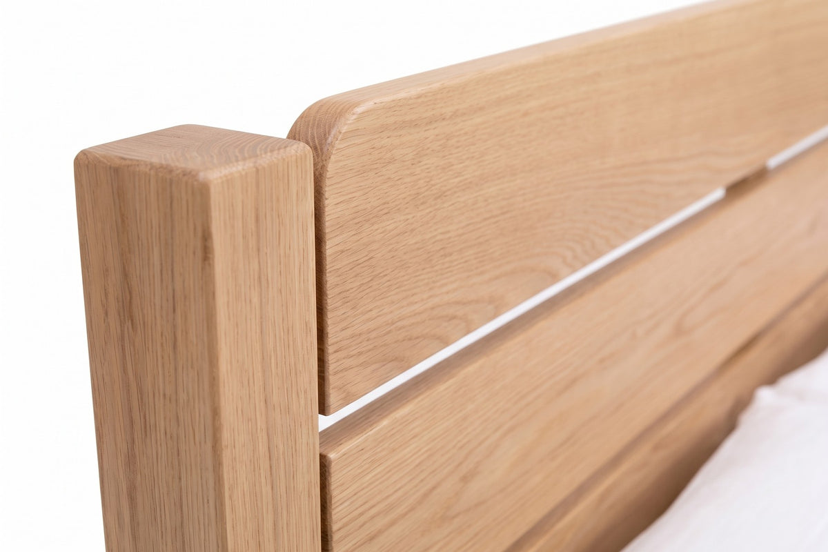 Sancerre Natural Oak Platform Bed: close-up of the headboard's top board with its softly rounded corner and the gap to the board below, showing the oak grain