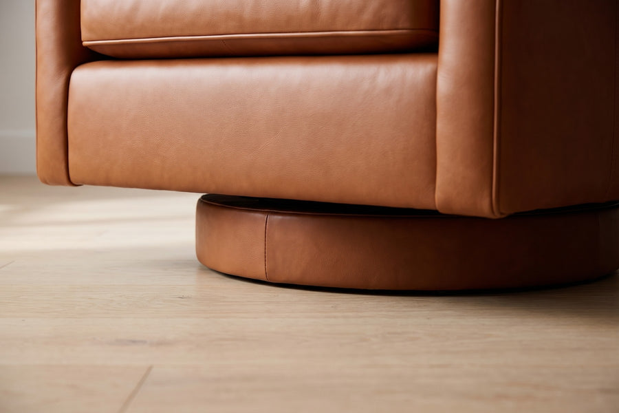 Sarlat Cognac Leather Swivel Club Chair: low close-up under the front of the chair, showing the round cognac leather plinth set back in shadow so the chair seems to float above a pale oak floor