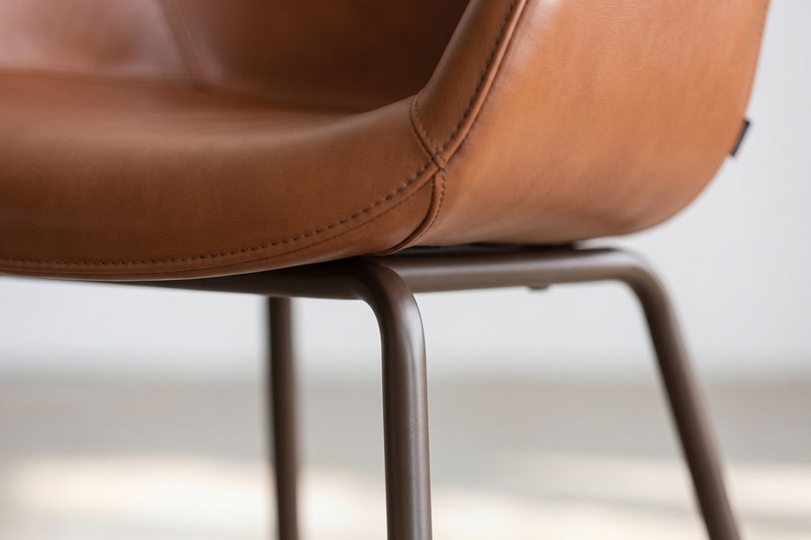 Saumur Cognac Leather Shell Dining Chair: close-up of where a slim dark bronze steel leg meets the underside of the leather shell