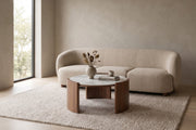 Sèvres 31.5" round white sintered stone coffee table with curved walnut legs in a calm, daylit living room in front of a sofa
