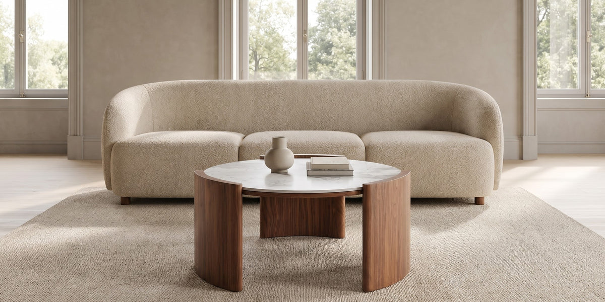 Sèvres 31.5" round white sintered stone coffee table with curved walnut legs in a wide room view