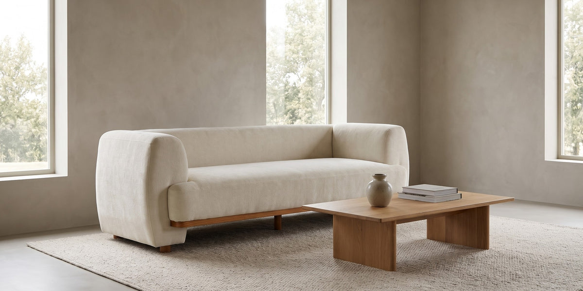 Solange 79" beige chenille sofa with rounded arms and wood base trim in a wide room view