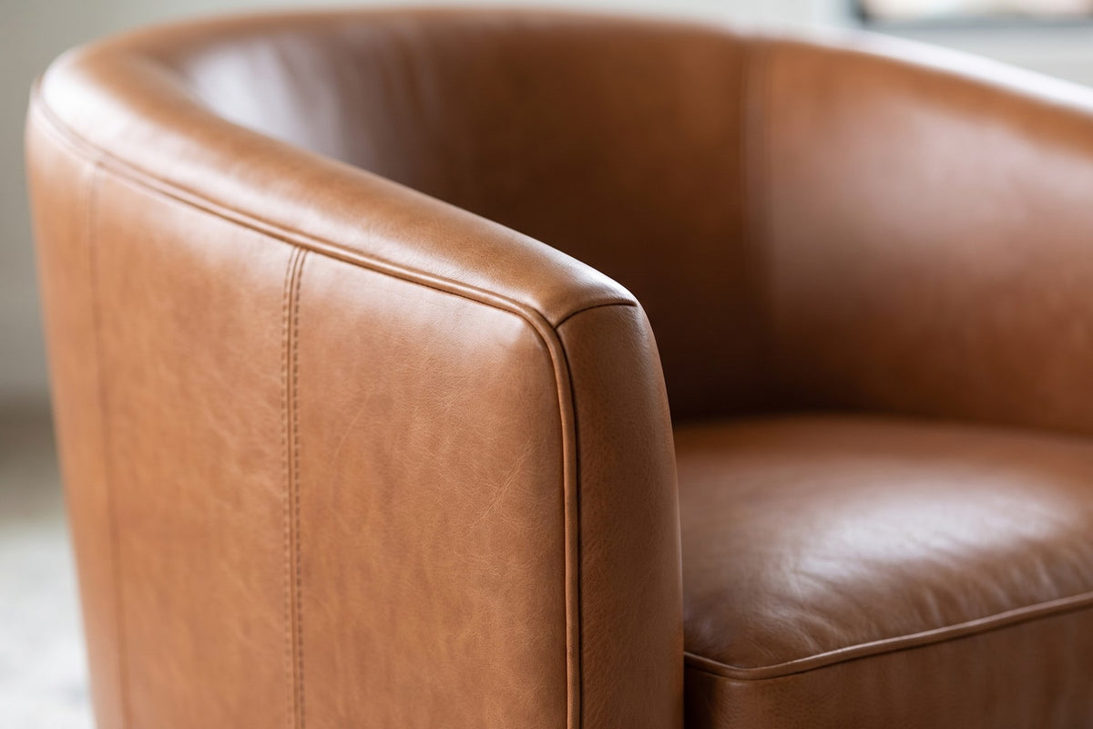 Solène Cognac Leather Swivel Chair: close-up of the cognac leather where the curved back meets the arm, showing a stitched panel seam, the leather grain and its soft sheen