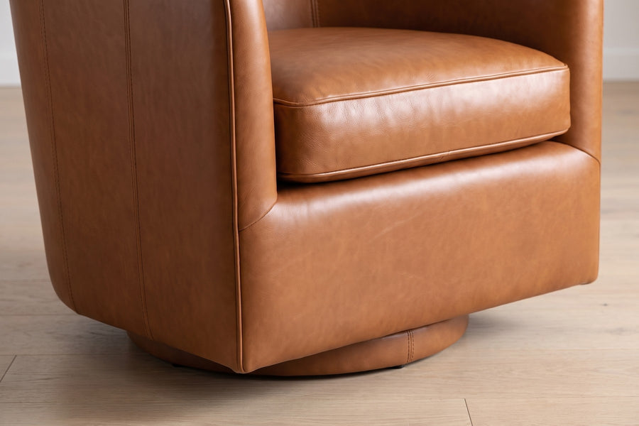 Solène Cognac Leather Swivel Chair: close-up of the seat cushion edge and the low recessed round base below it, the chair turned slightly, on a pale oak floor