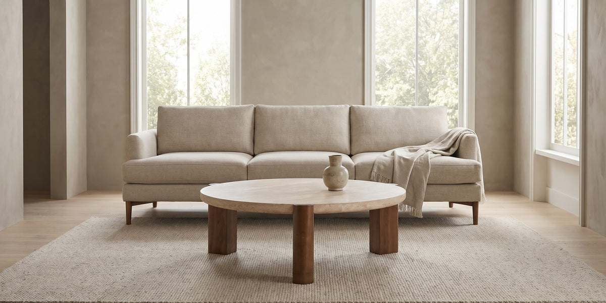 Suzanne 40" round travertine coffee table with dark oak-veneer legs in a wide room view