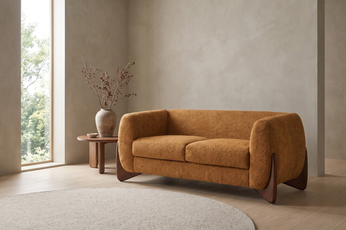 In a quiet plaster-walled room, the caramel bouclé rests on sculpted dark wood feet.