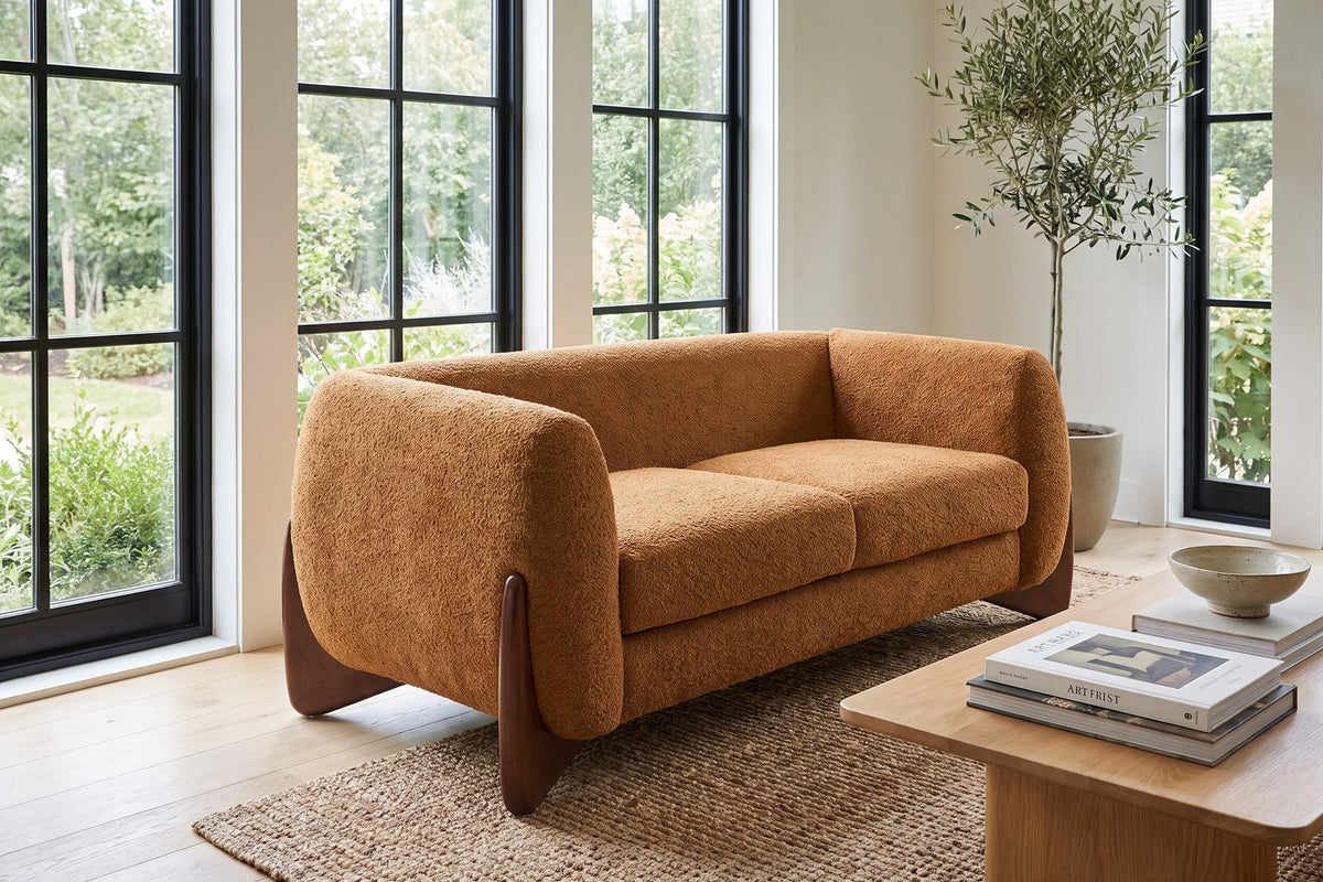 Trocadéro caramel bouclé loveseat with sculpted wood wedge feet in a bright sunroom-style living room
