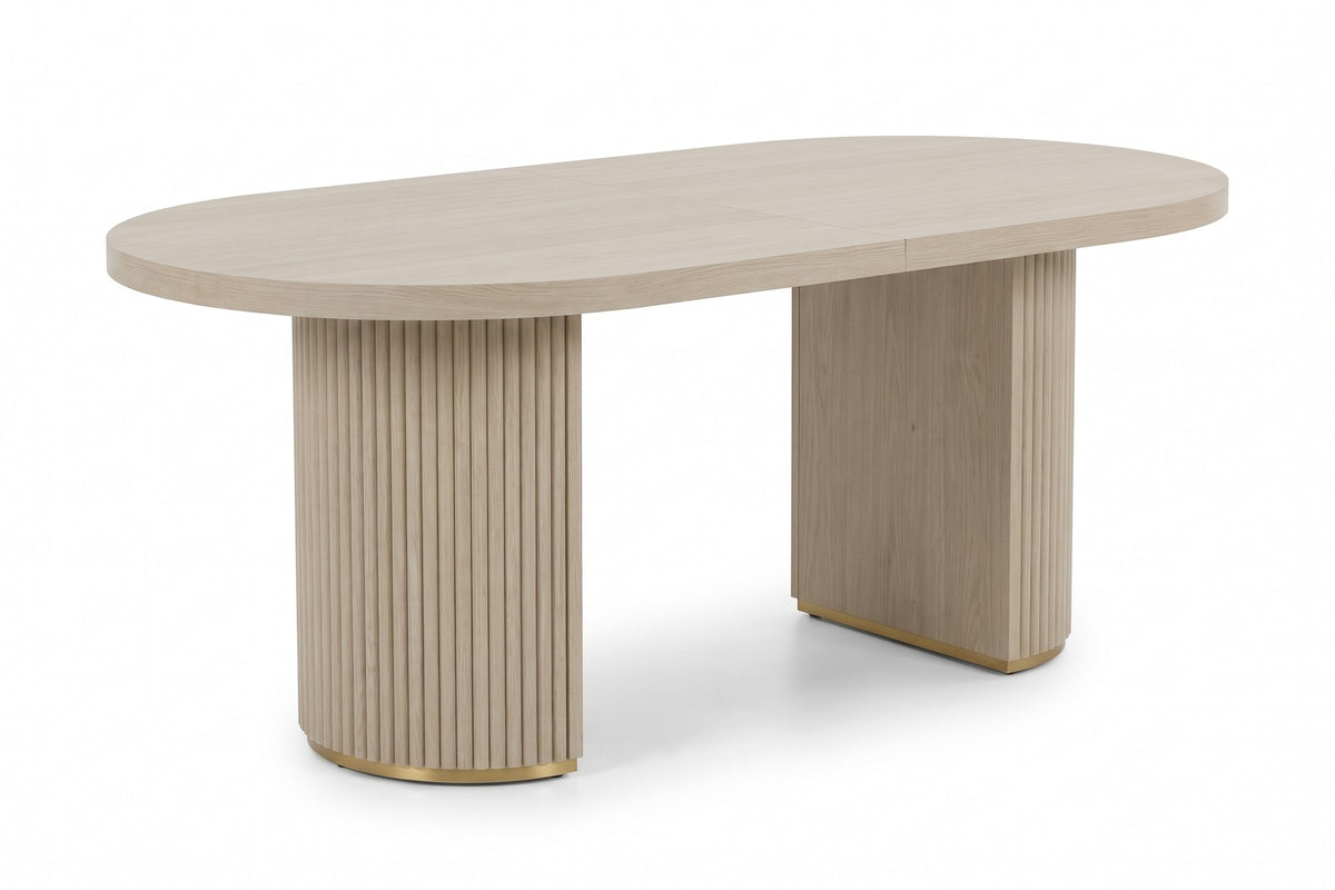 Tuileries 88-inch oval dining table with two fluted pedestals in a light natural finish, end view along the short side, showing the curved fluted face of the near pedestal under the rounded end of the top on a white background