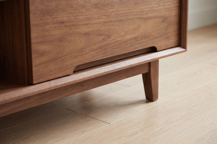 Valence Walnut Media Console: close-up of the slim base frame and one short tapered leg under a front corner, above a pale oak floor