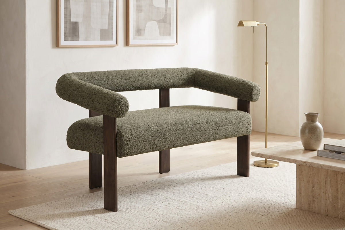 Daylight. Under framed prints, the round bolster arms and back read soft and sculptural.